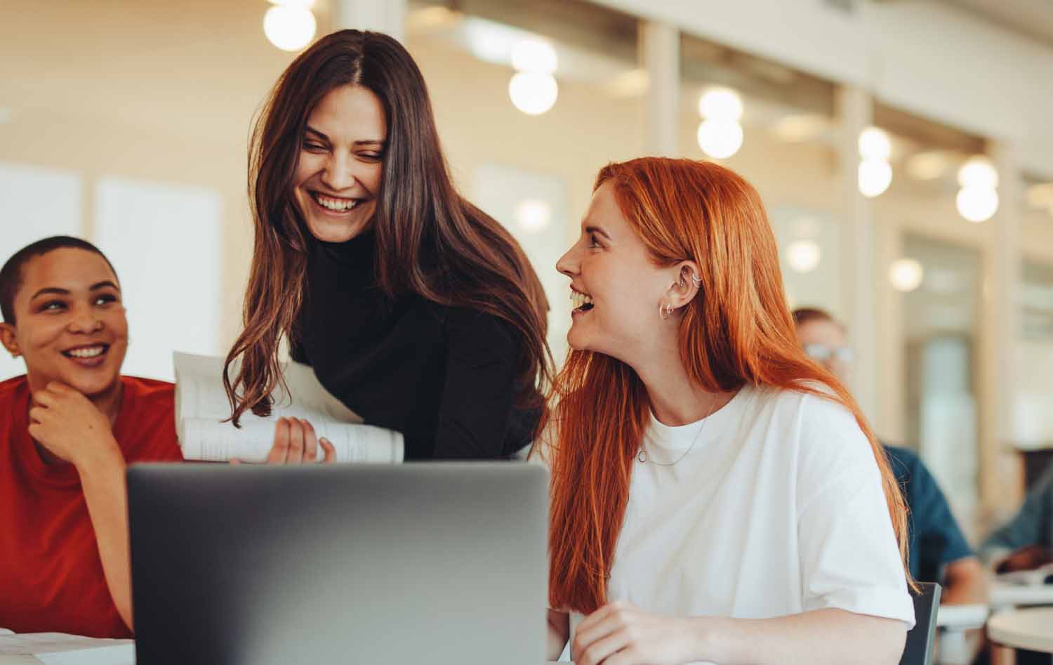 A smiling female lecturer with two female students at a laptop