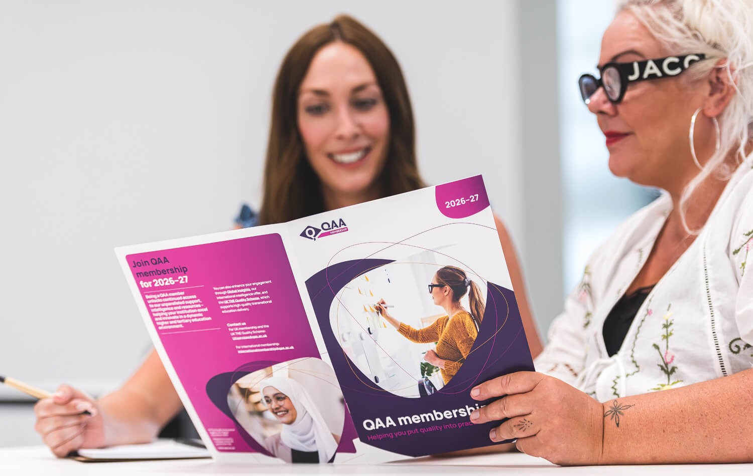 Two QAA colleagues reading the membership  brochure