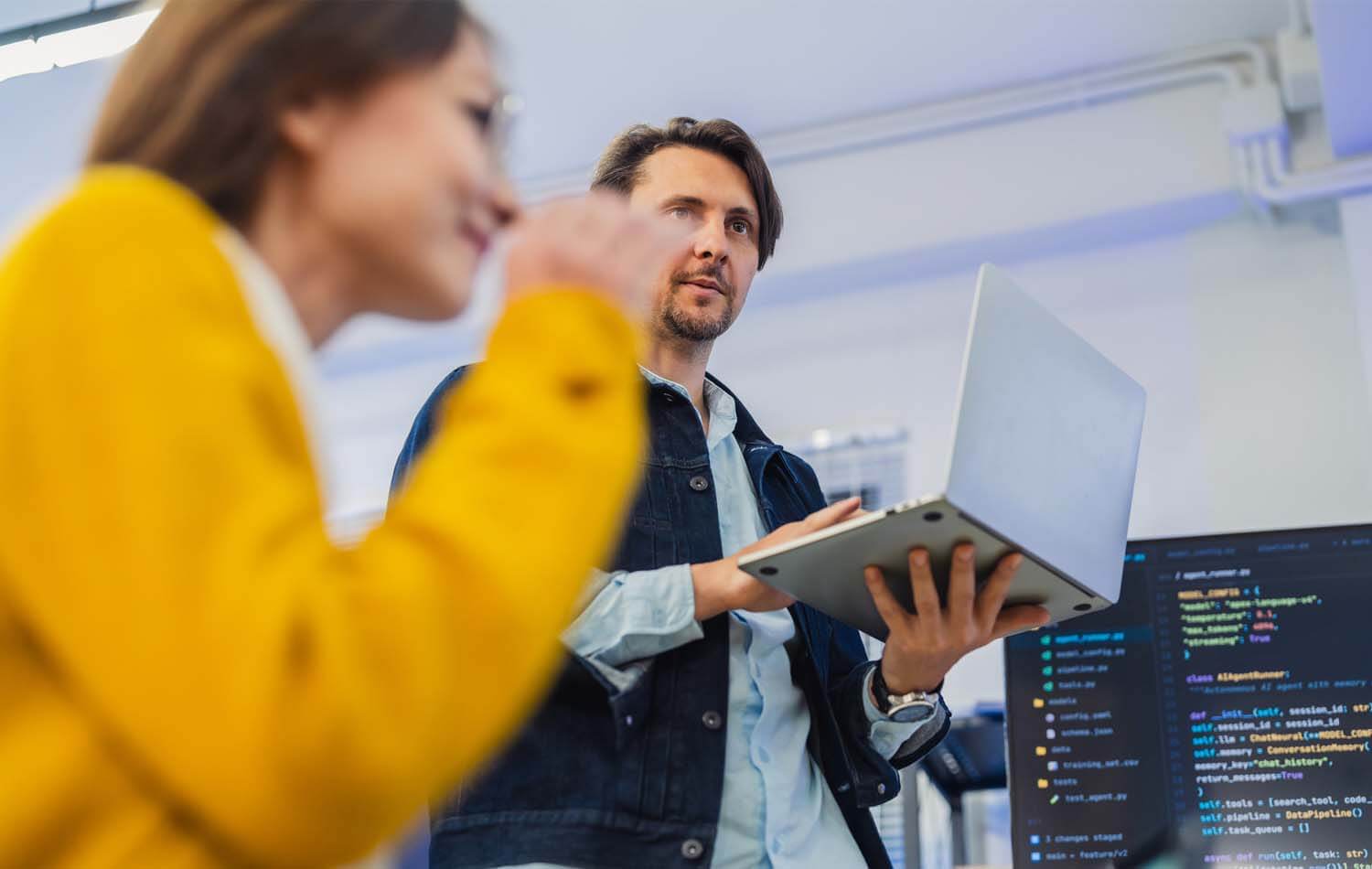 Female AI team leader presents to developers on office monitor.